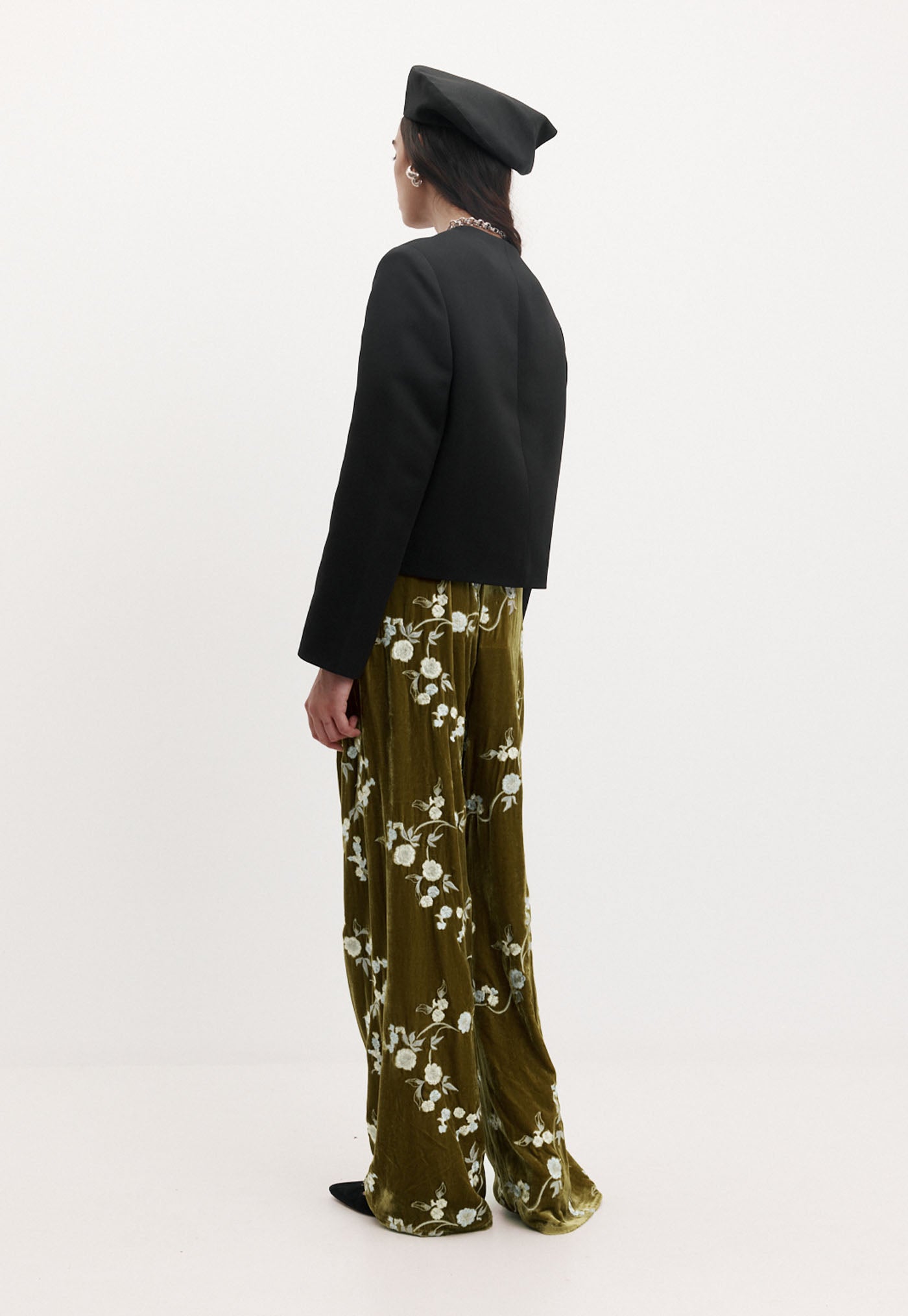 Person wearing a black coat and green floral pants on a white background