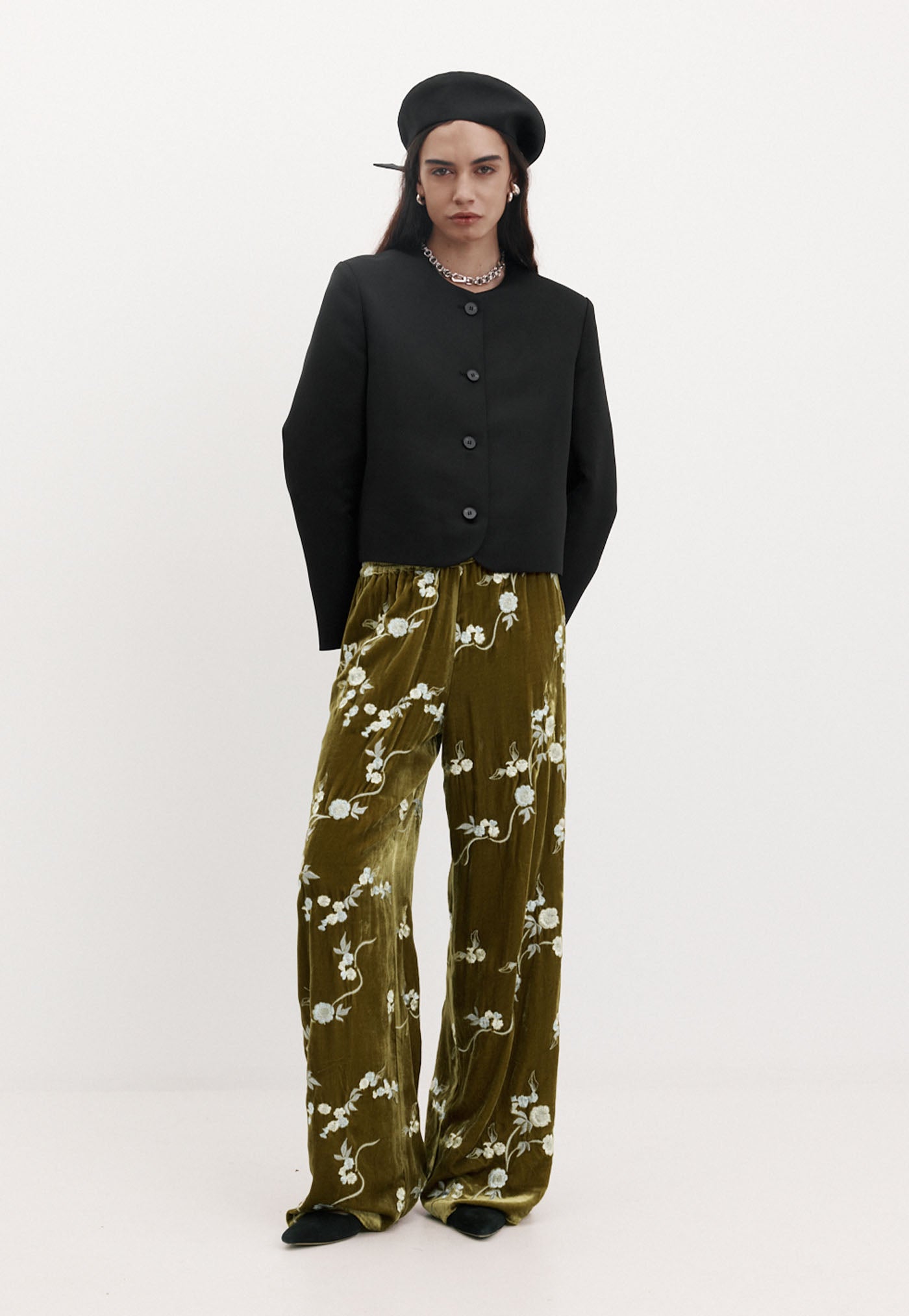 Person wearing a black jacket and green floral pants on a white background