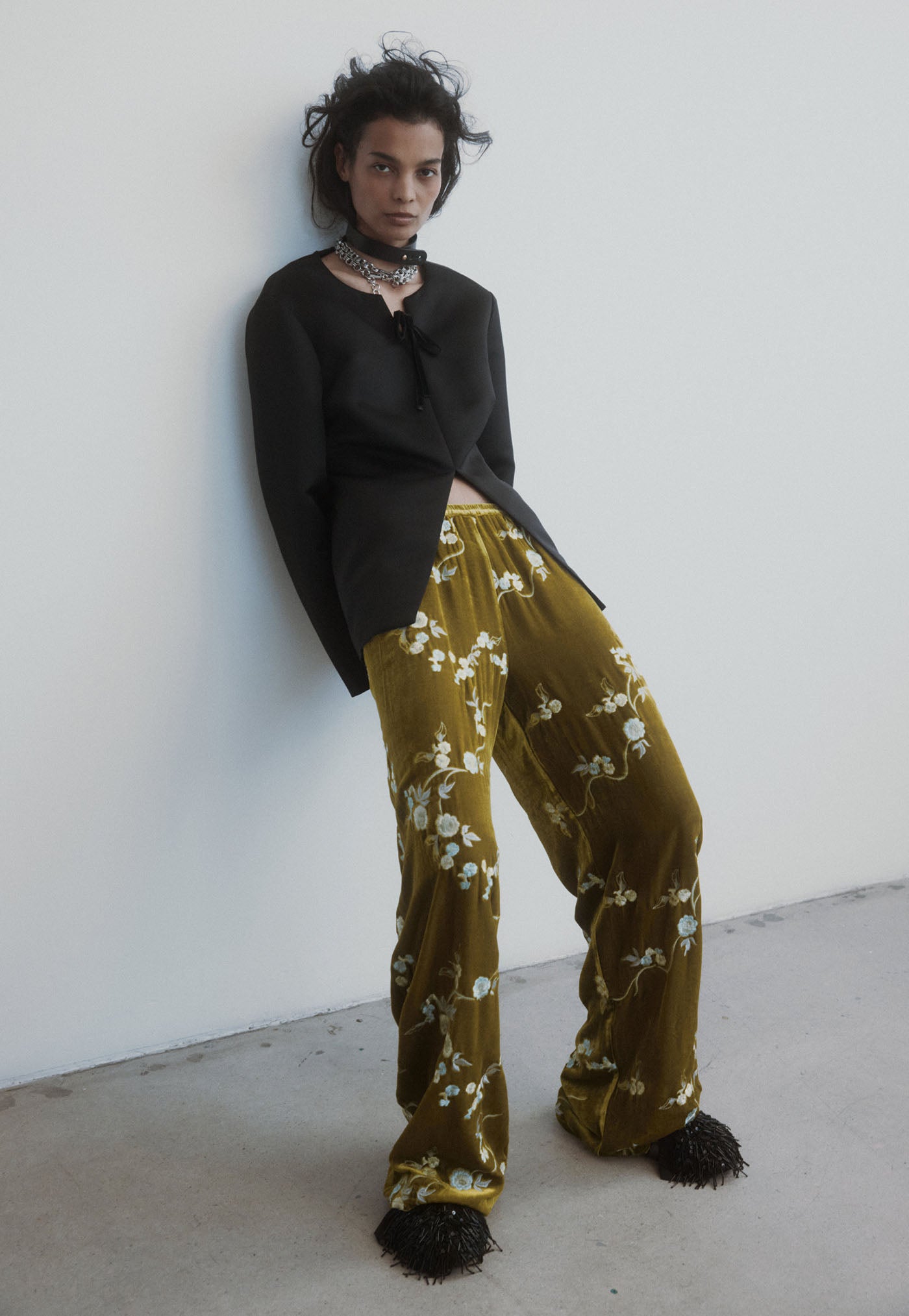 Person wearing a black top and green floral pants against a white wall.