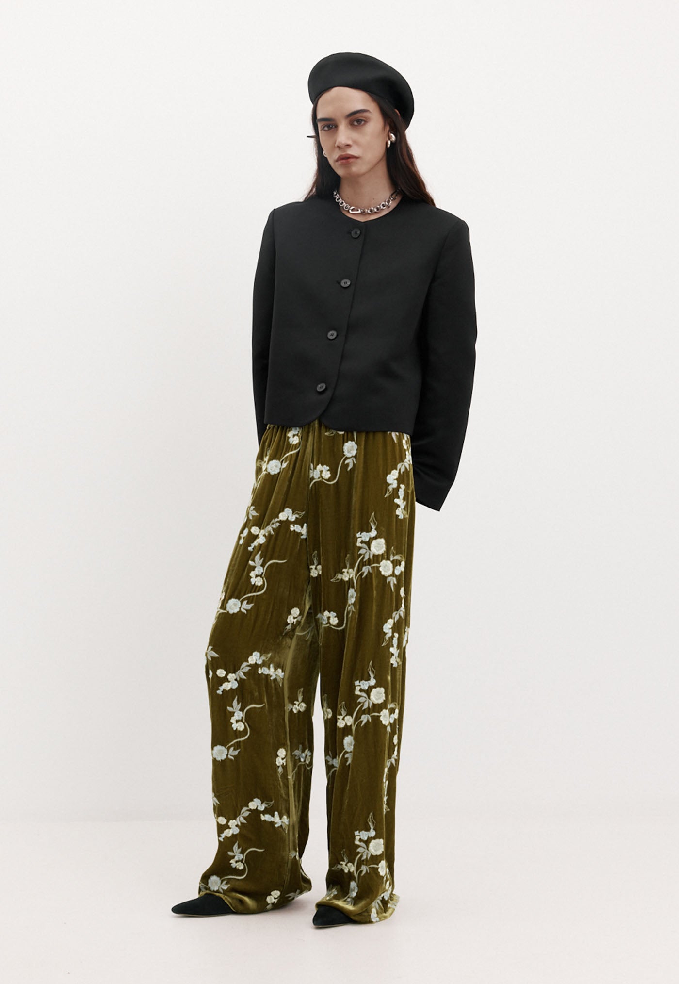 Person wearing a black outfit with floral-patterned pants on a white background